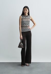 Πλεκτό αμάνικο τοπ με πολύχρωμο κυματιστό σχέδιο, συνδυασμένο με μαύρο παντελόνι καμπάνα. Η εμφάνιση ολοκληρώνεται με μια φλοράλ τσάντα και παπούτσια με λουράκια.