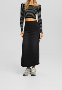 Czarna, dżinsowa maks spódnica z dopasowanym pasem, połączona z czarno-białą, off-shoulder bluzką i szarymi trampkami.