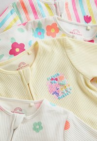 Quatre bodies bébé côtelés avec des imprimés floraux et en forme de cœur dans des couleurs pastel, avec des fermetures éclair à l'avant et des textures de tissu doux.