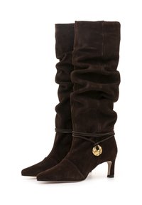 Botas de ante marrón hasta la rodilla con diseño recogido, punta afilada y un tacón corto. Presentan un acento decorativo en tono dorado y un detalle de cordón atado.