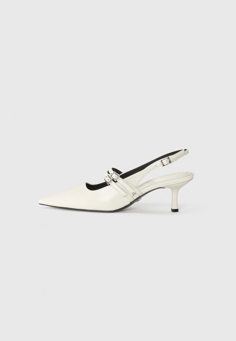 Chaussure à talon kitten en cuir blanc avec bride arrière, bout pointu, deux boucles latérales et talon fin sur un fond clair uni.