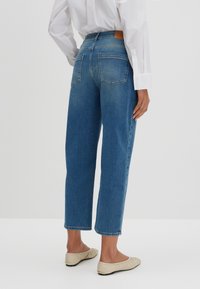 Jeans in denim blu con taglio dritto, vita medio-alta e tasche posteriori. Completati con un'etichetta in pelle in vita.