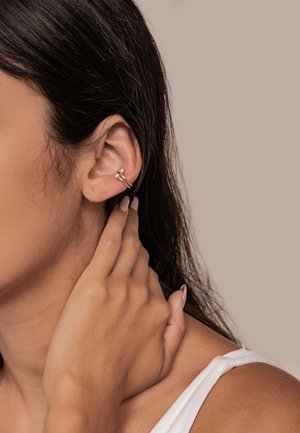 Gold-tone ear cuff featuring two interlocking rings with a smooth finish. Worn on the upper ear, with a minimalist design.