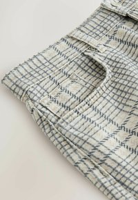 Detalje af beige og sort ternet stof med sydd syning og lille rektangulært lomme-detalje.