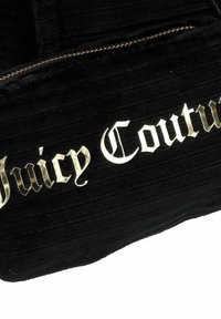 Zwarte fluwelen tas met geprofileerde textuur, voorzien van het gouden "Juicy Couture"-logo in een decoratieve lettertype en een ritssluiting.