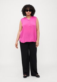 Top senza maniche di un vivace colore rosa con scollatura a V e tre bottoni, abbinato a pantaloni neri larghi e ballerine nere. Tessuto morbido, vestibilità casual.