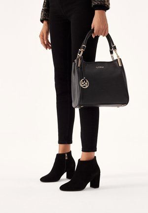 Borsa nera in pelle con finitura strutturata, dettagli in metallo dorato e ciondolo con logo, abbinata a stivaletti neri in camoscio con tacco a blocco.