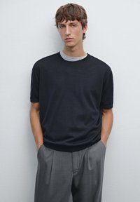 Men's short-sleeve crew neck sweater in black with grey accents, made of soft fabric, paired with light grey tailored trousers.