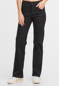 Zwarte denim jeans met een rechte snit, vijf zakken en metalen knoopsluiting. Draagt een paar witte sneakers.