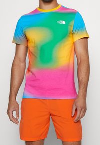 Mehrfarbiges T-Shirt mit einem verlaufenden Design in Blau, Grün, Pink und Gelb, kombiniert mit orangefarbenen Shorts; aus weichem Stoff gefertigt.