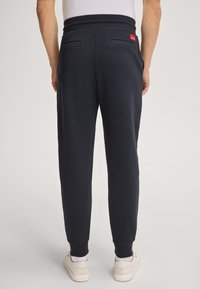 Marineblaue Jogginghosen aus weichem Stoff, mit gerippten Bündchen, seitlichen Taschen und einem kleinen roten Etikett am Bund.