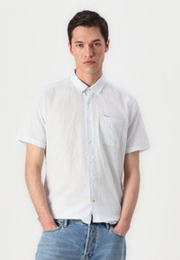 Camisa de manga curta, azul clara, com um padrão texturizado, colarinho abotoado, bolso frontal e uma marcação discreta. O tecido parece leve e respirável.