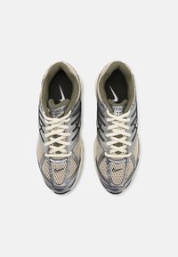 Zapatillas de running beige y gris con parte superior de malla, acentos reflectantes y cordones blancos. Logo de la marca presente en los lados y en la lengua.