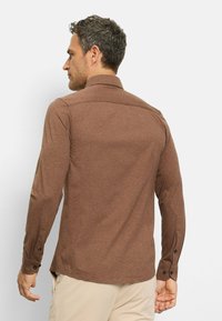 Braunes Langarmhemd mit klassischem Kragen, Knopfmanschetten und strukturiertem Stoff. Die Rückansicht zeigt ein tailliertes Design und seitliche Schlitze.