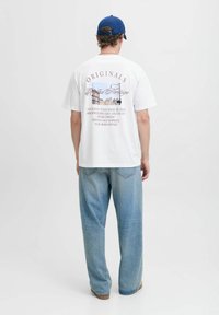 Maglietta bianca a maniche corte con una stampa grafica sul retro, con testo in diversi caratteri e colori. Abbinata a jeans a gamba larga di colore blu chiaro.