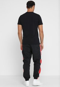 Černé tričko s krátkým rukávem spárované s černými teplákovými kalhotami s červenými postranními pruhy, doplněné bílými teniskami. Jednoduchý a funkční design.