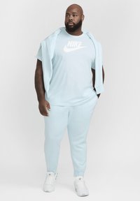 Sudadera y chándal Nike de color azul claro, tejido suave, corte holgado, logo grande en la camiseta, complementado con zapatillas blancas.