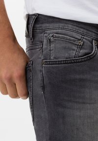 Faded black denim jeans with a slim fit, five pockets, and metal hardware accents. The texture is smooth with subtle wear patterns.