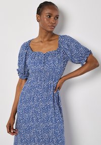 Vestido azul con escote cuadrado, mangas abullonadas y cintura entallada. Presenta un patrón blanquecino a rayas en toda su superficie. Textura de tela suave.