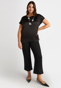 Svart satinskjorta med korta ärmar, ihopparad med svarta cropped-byxor och spetsiga svarta slingback-klackar. Anmärkningsvärd silverkedja som halsband.