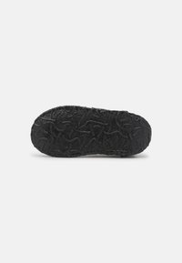 Black rubber shoe sole with textured surface, featuring swirling patterns for improved grip. Rounded shape with a flat profile.