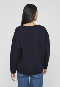 Sudadera navy de gran tamaño con mangas largas, puños acanalados y un escote ancho, sobre un fondo claro liso.