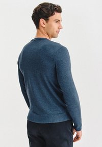 Granatowy sweter z długim rękawem i okrągłym dekoltem, wykonany z miękkiego materiału, charakteryzujący się dopasowanym krojem oraz ściągaczami przy mankietach i u dołu.