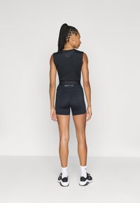 Top fără mâneci Nike Pro negru și pantaloni scurți mulați, având un spate texturat, talie branduită și asortați cu șosete albe și adidași negri.