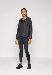 Black lightweight running jacket with zipper, paired with a black short-sleeve top and black leggings. All items feature a logo accent.