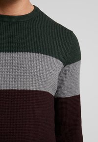 Gestrickter Pullover mit horizontalen Streifen in Dunkelgrün, Grau und Burgunderrot, strukturierter Oberfläche und rundem Halsausschnitt.