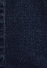 Dunkelblauer Denim-Stoff mit glatter Textur und sichtbarem diagonalen Webmuster. Die Kanten weisen leichte Fransen auf.