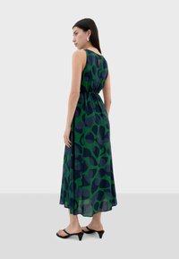 Abito maxi con un motivo astratto di foglie verde e blu navy, realizzato in tessuto leggero, con una vita aderente e design senza maniche.