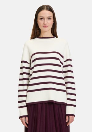 Maglione lavorato a maglia color crema con strisce orizzontali bordeaux, collo rotondo, vestibilità morbida e polsini a coste. Abbinato a una gonna plissettata scura.