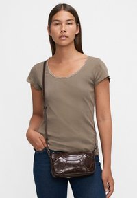 Borsa a tracolla in pelle marrone con una finitura testurizzata, caratterizzata da una forma strutturata e una tracolla regolabile, indossata con una t-shirt beige a coste.