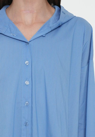 Camicia a scacchi blu con cappuccio, dotata di chiusura a bottoni e realizzata in tessuto morbido e leggero. Il motivo è composto da piccoli quadrati.