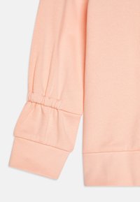 Világos barack színű pulóverujj puffadt, rugalmas mandzsettával és texturált anyaggal, sima felülettel és testhezálló fazonnal.