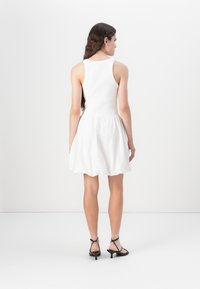White sleeveless dress with a fitted bodice and flared skirt. Textured cotton fabric. Black strappy heels complete the look. Rear view.