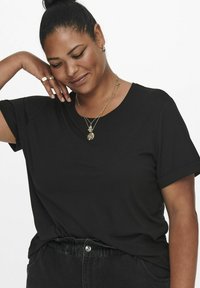 Black short-sleeve t-shirt in soft fabric, featuring a relaxed fit and rolled sleeves, paired with high-waisted dark jeans and layered necklaces.