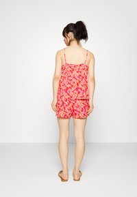 Macacão floral rosa com alças finas, apresentando um corte solto e calções com babados. Feito de um tecido leve, ideal para o clima quente.