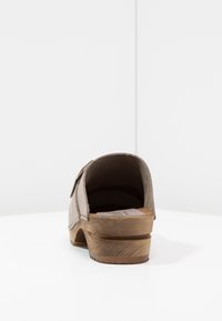 Sabots marron avec une semelle en bois, un dessus en daim et une seule sangle ajustable. Le talon est de forme bloc et l'intérieur n'est pas doublé.