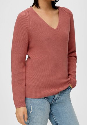 Maglione a maglia color ruggine con scollo a V, texture a coste, maniche lunghe e vestibilità leggermente ampia, abbinato a jeans chiari strappati.