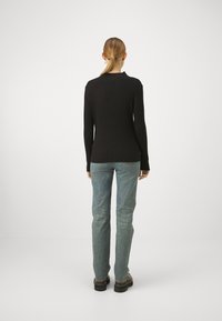 Černý žebrovaný top s dlouhým rukávem a přiléhavým střihem, kulatým výstřihem a texturovaným povrchem, kombinovaný s světlými rovnými džíny a robustními černými botami.