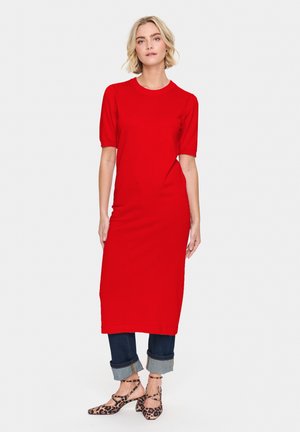 Red knit dress with short sleeves and a fitted silhouette, paired with cuffed dark jeans and leopard print ankle strap shoes.