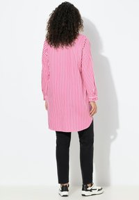 Roze-wit gestreept lang overhemd met een rechte snit en knoopmanchetten, gecombineerd met zwarte slim-fit broek en witte sneakers.