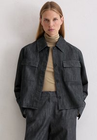 Ciemnoszara kurtka dżinsowa z kołnierzem, zapięciem na guziki z przodu, dwoma kieszeniami na piersi i luźnym fasonem, w połączeniu z beżowym golfem.