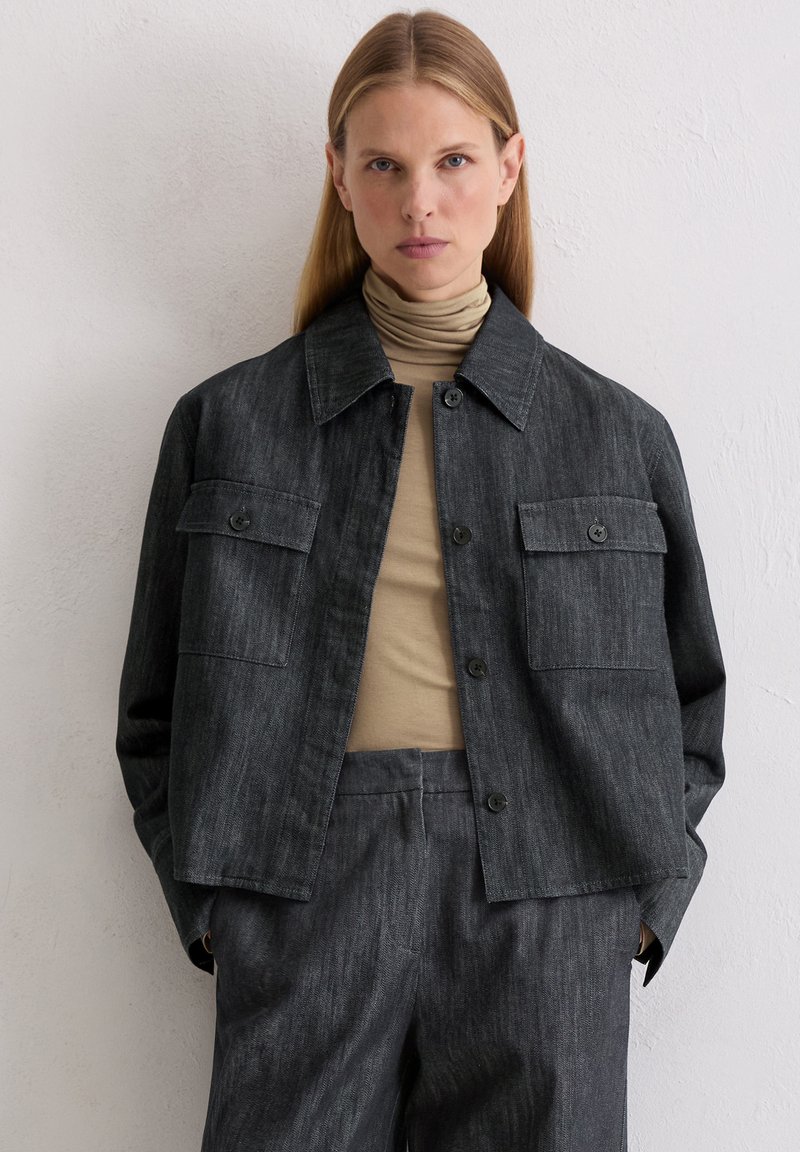 Ciemnoszara kurtka dżinsowa z kołnierzem, zapięciem na guziki z przodu, dwoma kieszeniami na piersi i luźnym fasonem, w połączeniu z beżowym golfem.