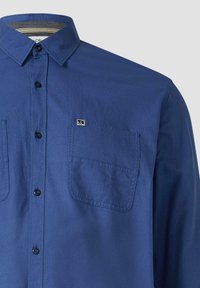 Blaues Hemd mit Knöpfen aus glattem Stoff, ausgestattet mit zwei Brusttaschen, einem spitzen Kragen und einem kleinen Logo auf der linken Seite.