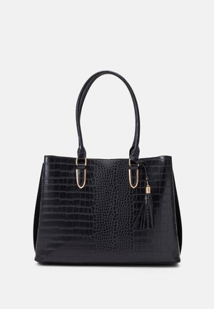 Bolso negro con textura de cocodrilo, dos correas para el hombro con detalles en dorado y un adorno de borla sobre un fondo liso.