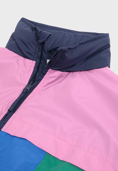 Kleurrijke windjack met een roze bovenstuk, blauw onderstuk en marineblauwe kraag. Gladde textuur met een volledige rits en naaddetails.