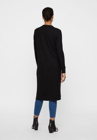 Svart långärmad klänning som når mitt på vaden, tillverkad av mjukt tyg. Kombinerad med blå jeans och ankellånga stövlar. Enkel, minimalistisk design.